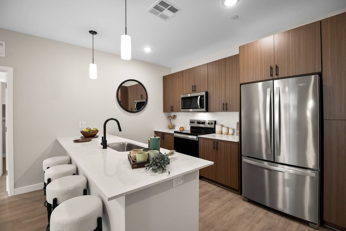 Origin Goodyear apartment kitchen with a large white island, wood cabinetry, pendant lighting, and stainless steel appliances.