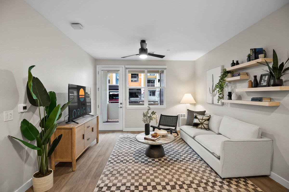 Origin Goodyear apartment living room with a sofa, lounge chair, television, plants, and access to a private balcony.