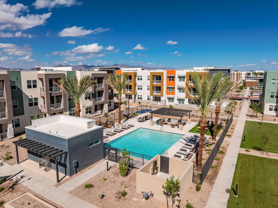 Aerial view of a modern apartment complex with a central outdoor pool, palm trees, and lounge chairs.